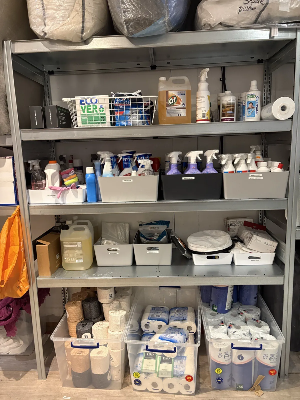 The supplies wall after: a metal shelving unit with labelled grey trays and boxed paper rolls
