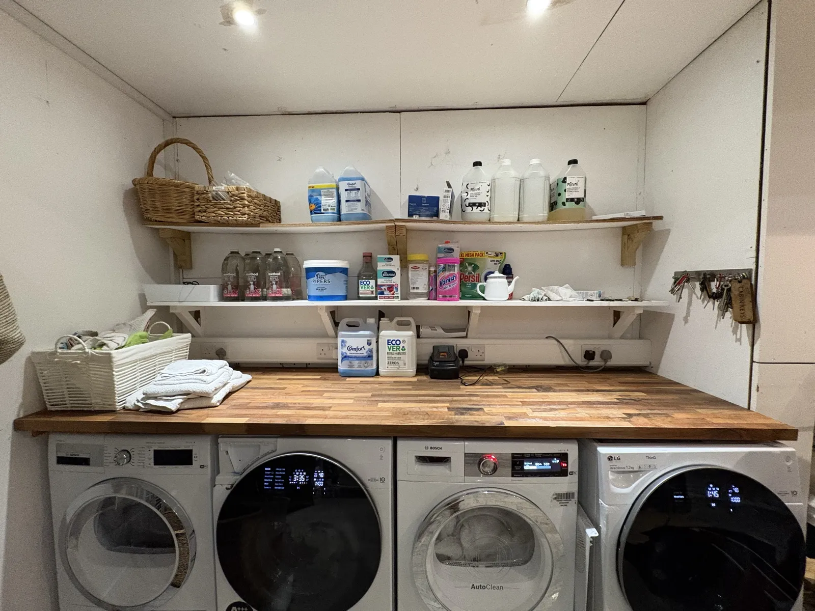 The laundry worktop after: the same machines with a clear wooden worktop and tidy, labelled shelves