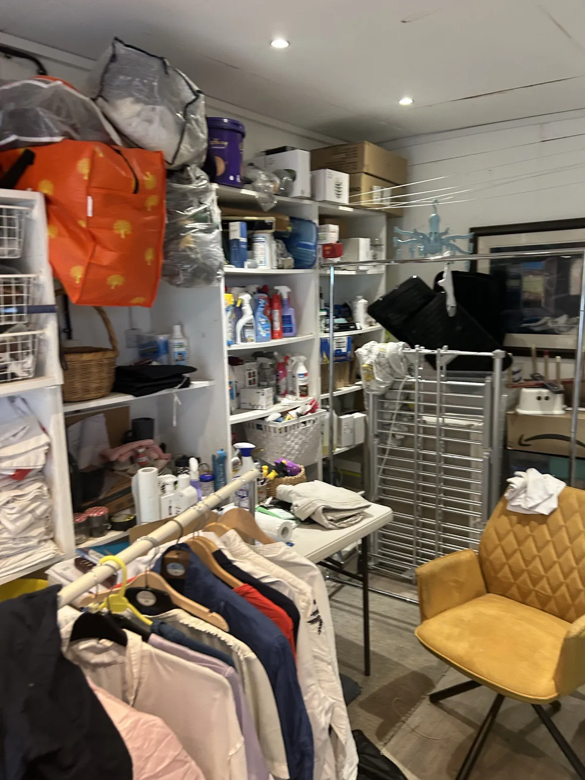 The supplies wall before: shelves of products and a clothes rail piled high
