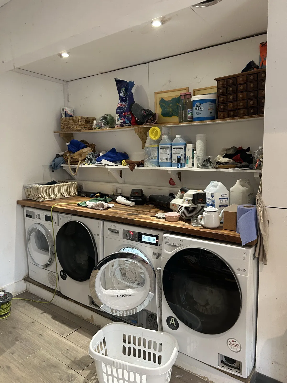 The laundry worktop before: four machines under a cluttered worktop and two shelves